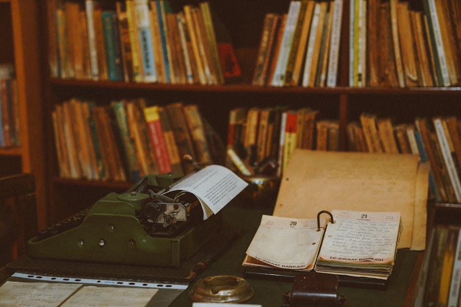 A vintage typewriter and notebooks sit on a desk in a cozy library filled with books.