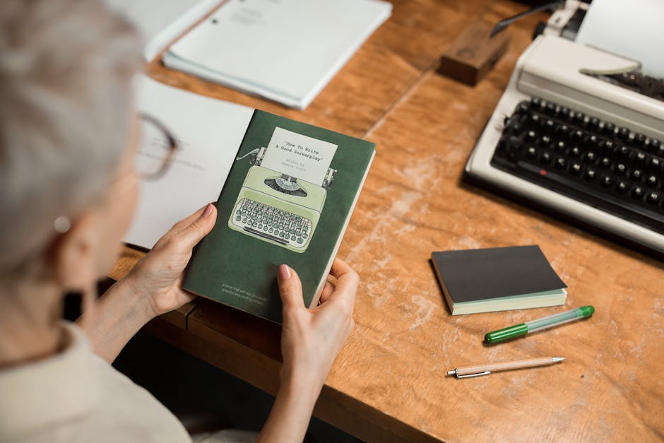 Elderly woman holding a book at a wooden desk with a classic typewriter, creating a retro office vibe.